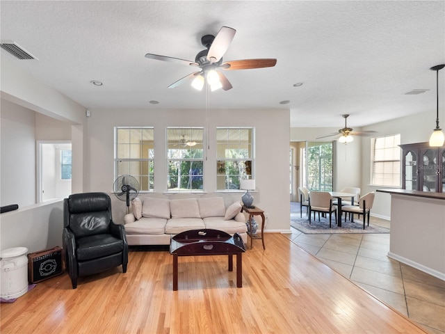 living room featuring a textured ceiling, light wood-type flooring, and ceiling fan