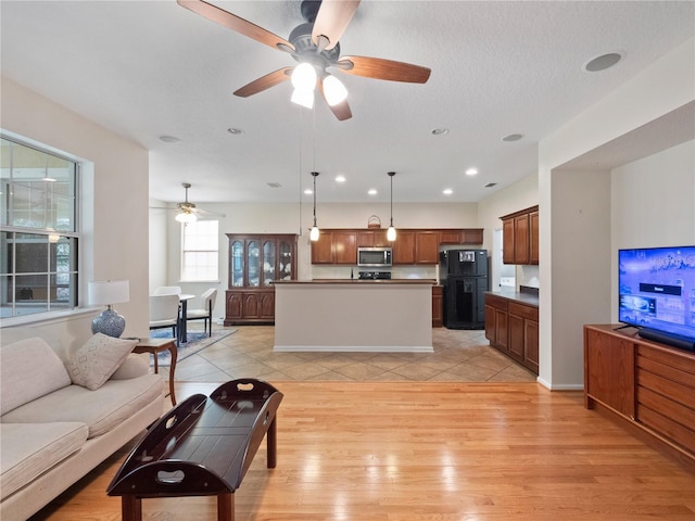 living room with ceiling fan, a textured ceiling, and light wood-type flooring