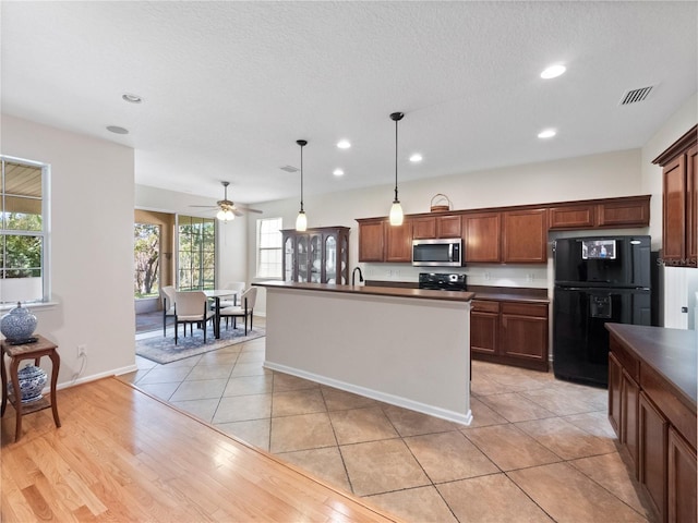 kitchen featuring black appliances, ceiling fan, light wood-type flooring, an island with sink, and decorative light fixtures