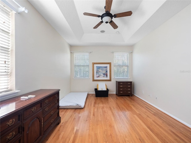 living area with light wood-type flooring, a raised ceiling, and ceiling fan