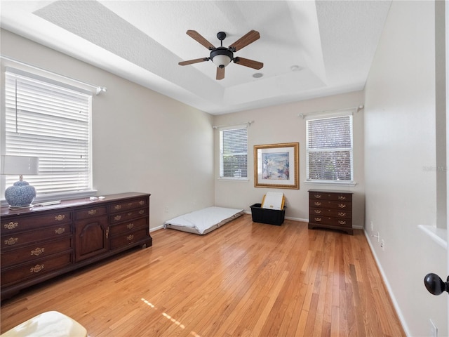 unfurnished bedroom featuring ceiling fan, light wood-type flooring, a textured ceiling, and a tray ceiling