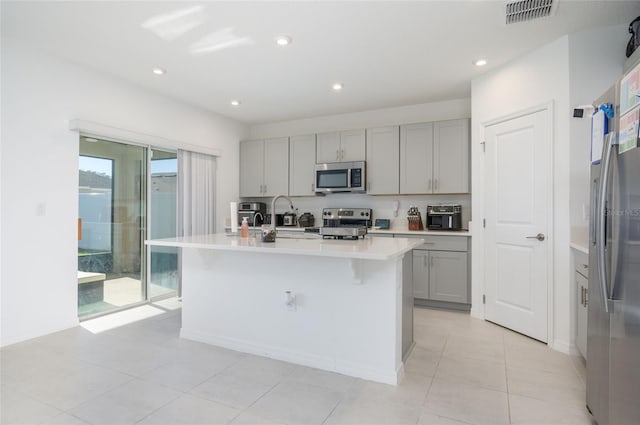 kitchen with sink, gray cabinets, light tile patterned floors, an island with sink, and appliances with stainless steel finishes