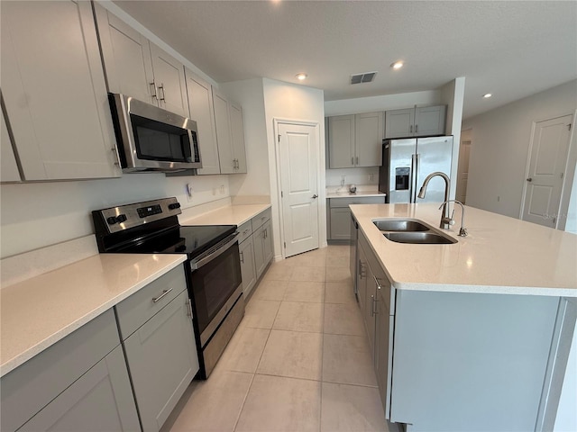 kitchen featuring an island with sink, sink, gray cabinetry, light tile patterned floors, and stainless steel appliances