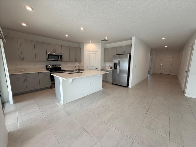 kitchen with gray cabinetry, sink, a center island with sink, and appliances with stainless steel finishes