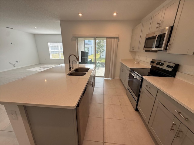 kitchen with a center island with sink, appliances with stainless steel finishes, sink, and light tile patterned floors