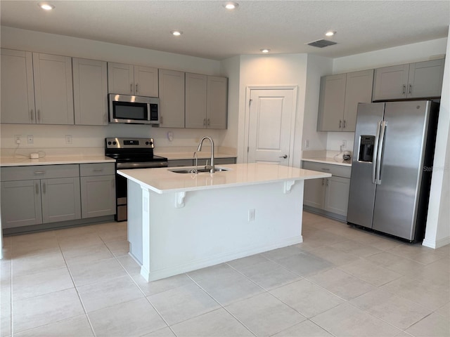 kitchen featuring gray cabinets, appliances with stainless steel finishes, sink, and a center island with sink