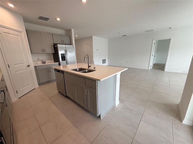 kitchen with sink, gray cabinetry, light tile patterned floors, an island with sink, and stainless steel appliances