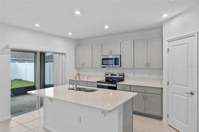 kitchen with sink, gray cabinetry, a center island with sink, light tile patterned floors, and stainless steel appliances