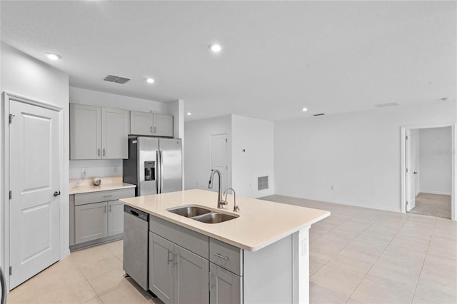 kitchen featuring sink, gray cabinetry, stainless steel appliances, an island with sink, and light tile patterned flooring