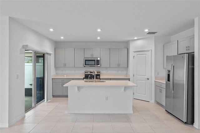 kitchen featuring a kitchen bar, sink, gray cabinetry, appliances with stainless steel finishes, and a kitchen island with sink