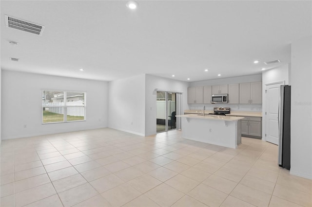 kitchen featuring sink, a center island with sink, light tile patterned floors, gray cabinets, and stainless steel appliances