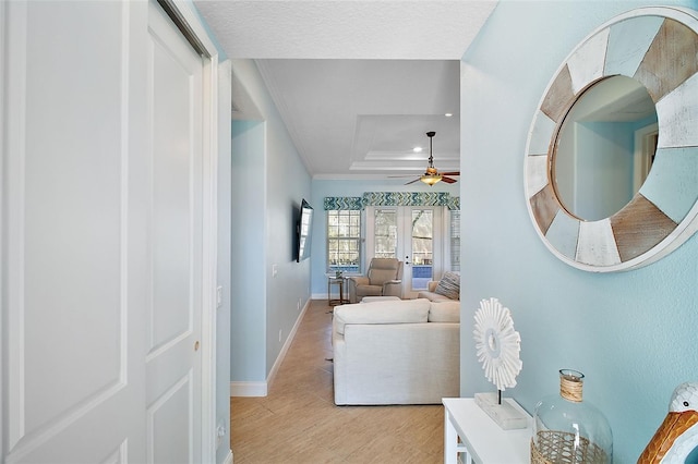 living room with ceiling fan, french doors, a raised ceiling, crown molding, and light hardwood / wood-style floors