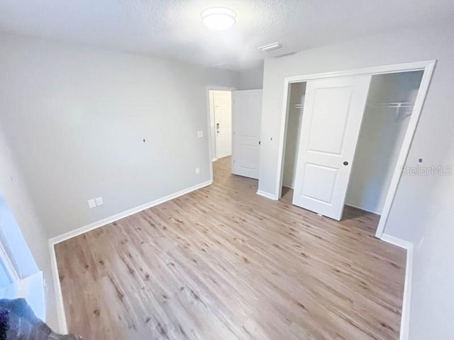 unfurnished bedroom with a textured ceiling, light hardwood / wood-style flooring, and a closet