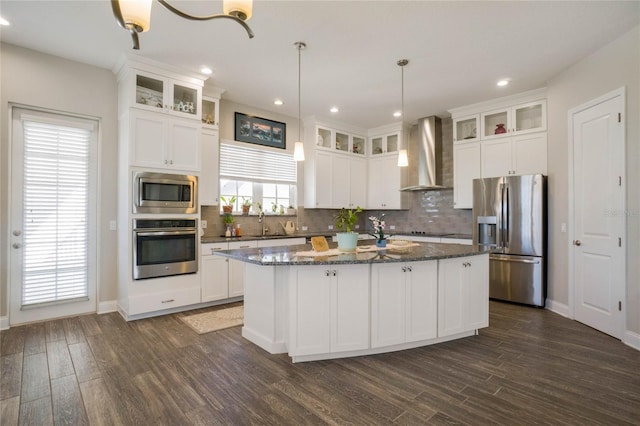 kitchen featuring a kitchen island with sink, hanging light fixtures, wall chimney exhaust hood, dark hardwood / wood-style floors, and appliances with stainless steel finishes