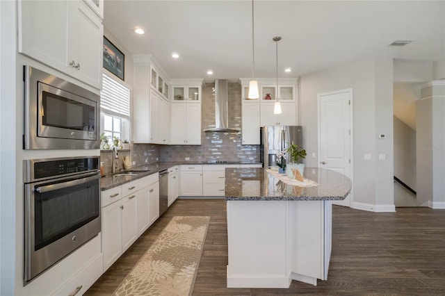 kitchen featuring a center island, wall chimney range hood, stainless steel appliances, and white cabinetry