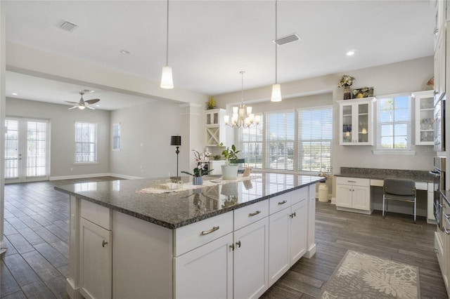 kitchen featuring ceiling fan with notable chandelier, a kitchen island with sink, dark wood-type flooring, dark stone countertops, and white cabinets