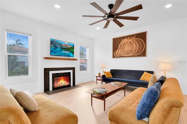 living room featuring ceiling fan, light wood-type flooring, and a brick fireplace