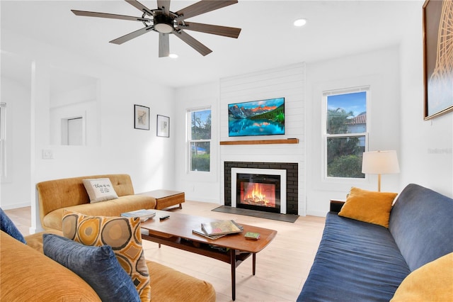 living room with ceiling fan, light hardwood / wood-style floors, and a brick fireplace