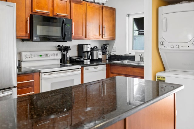 kitchen with white appliances, stacked washing maching and dryer, dark stone counters, and sink