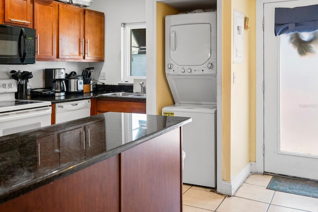 kitchen with sink, stacked washer / dryer, dark stone counters, white appliances, and light tile patterned flooring