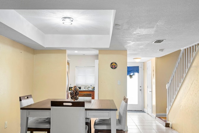 tiled dining space with a textured ceiling and a raised ceiling