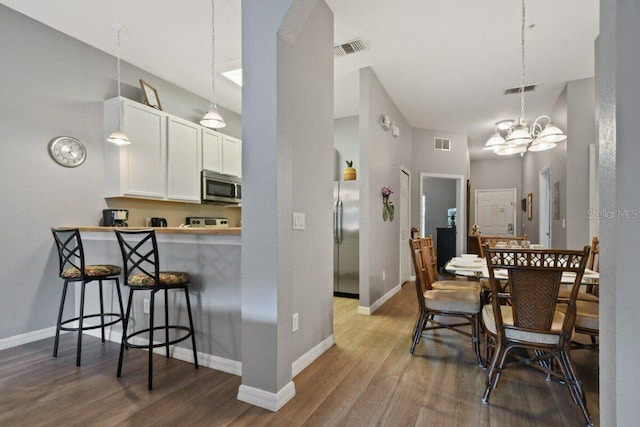 kitchen with white cabinetry, a notable chandelier, hardwood / wood-style floors, a kitchen bar, and appliances with stainless steel finishes