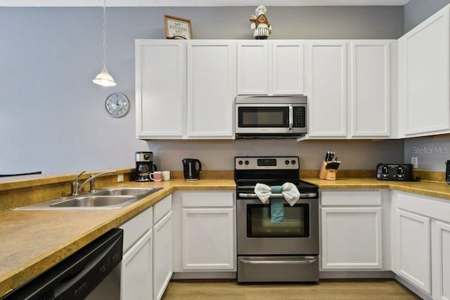 kitchen with white cabinets, light hardwood / wood-style floors, stainless steel appliances, and hanging light fixtures