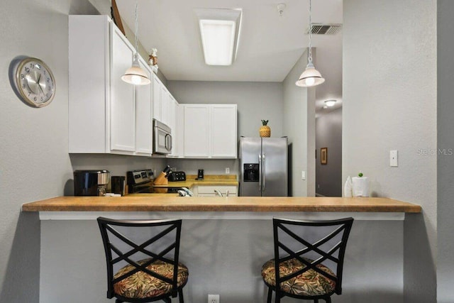 kitchen featuring a kitchen breakfast bar, kitchen peninsula, decorative light fixtures, white cabinetry, and stainless steel appliances