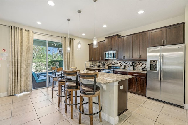 kitchen with light stone countertops, appliances with stainless steel finishes, a center island with sink, decorative light fixtures, and a breakfast bar area