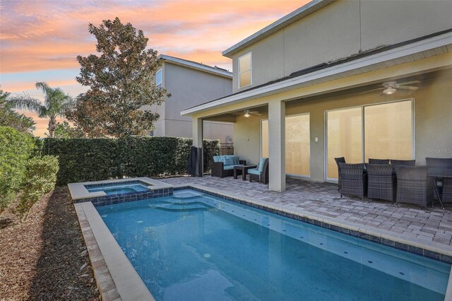 pool at dusk with an in ground hot tub, an outdoor hangout area, ceiling fan, and a patio area