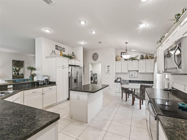 kitchen featuring washing machine and clothes dryer, stainless steel appliances, a kitchen island, vaulted ceiling, and white cabinets