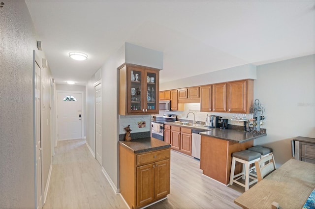 kitchen with decorative backsplash, brown cabinets, a peninsula, stainless steel appliances, and a sink