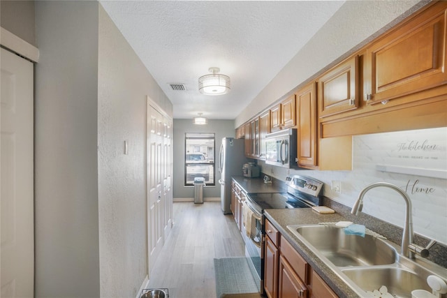 kitchen featuring sink, light hardwood / wood-style flooring, a textured ceiling, and appliances with stainless steel finishes