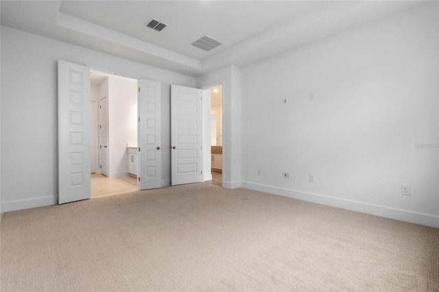 unfurnished bedroom with light colored carpet, a raised ceiling, and ensuite bath