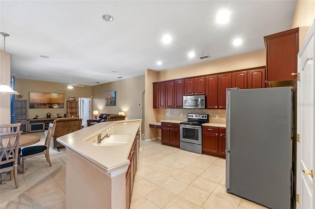 kitchen with ceiling fan, appliances with stainless steel finishes, tasteful backsplash, a kitchen island with sink, and sink