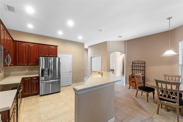 kitchen with light tile patterned floors, stainless steel appliances, a kitchen island with sink, pendant lighting, and sink