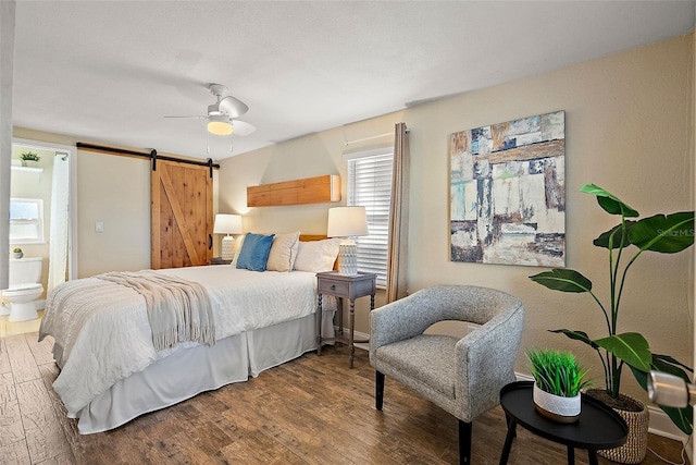 bedroom with hardwood / wood-style floors, a barn door, ensuite bathroom, and ceiling fan