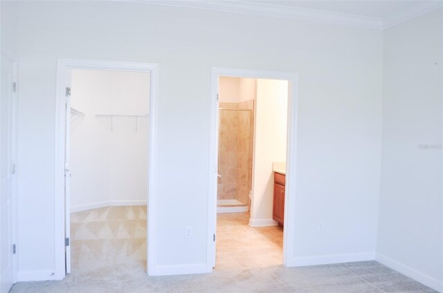 unfurnished bedroom with ensuite bathroom, a walk in closet, crown molding, light colored carpet, and a closet