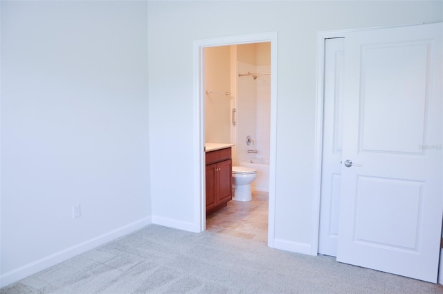 unfurnished bedroom featuring light carpet, ensuite bathroom, and a spacious closet