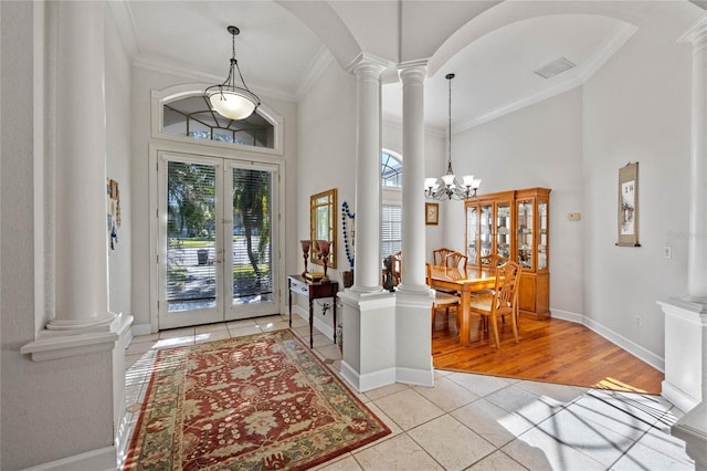 foyer featuring french doors, a towering ceiling, crown molding, light hardwood / wood-style flooring, and a chandelier