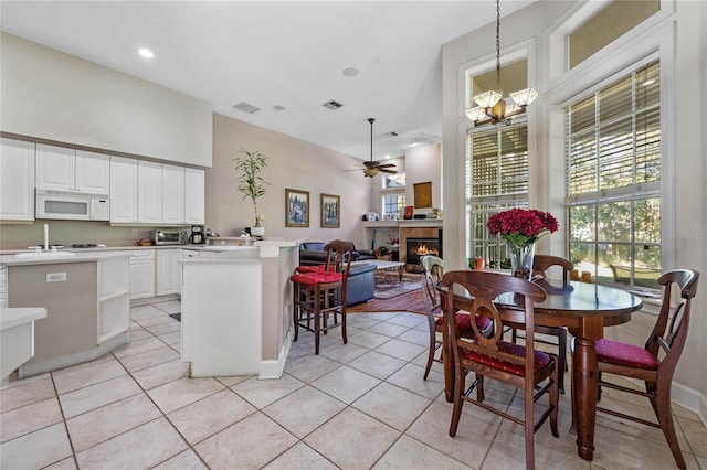 dining room featuring ceiling fan with notable chandelier, light tile patterned floors, and a tiled fireplace