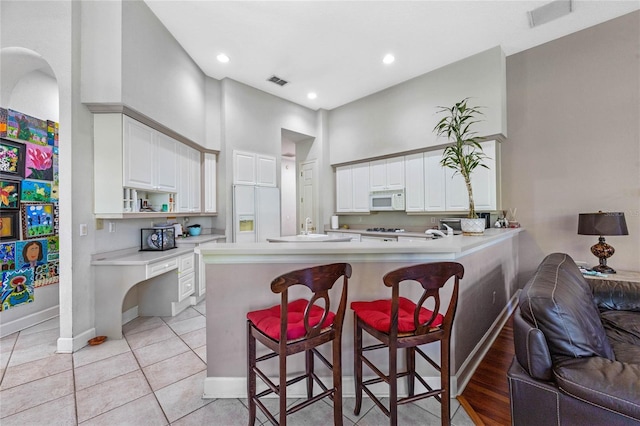 kitchen with white cabinets, kitchen peninsula, white appliances, a breakfast bar area, and light tile patterned floors