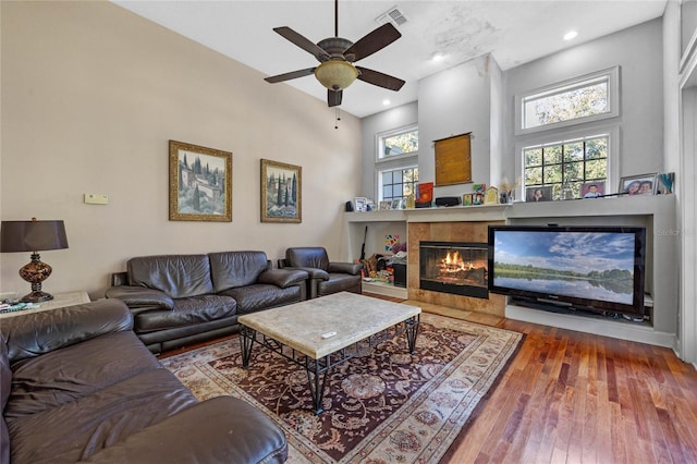 living room with ceiling fan, a fireplace, wood-type flooring, and a high ceiling