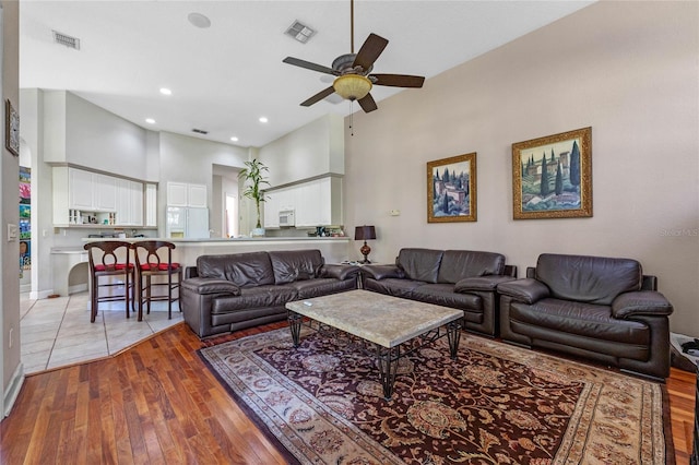 living room with ceiling fan, wood-type flooring, and a high ceiling