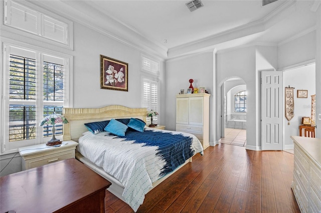 bedroom with hardwood / wood-style floors, ensuite bath, multiple windows, and ornamental molding