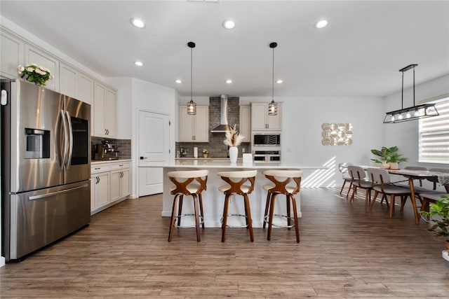 kitchen featuring a center island with sink, decorative light fixtures, wall chimney range hood, and stainless steel appliances