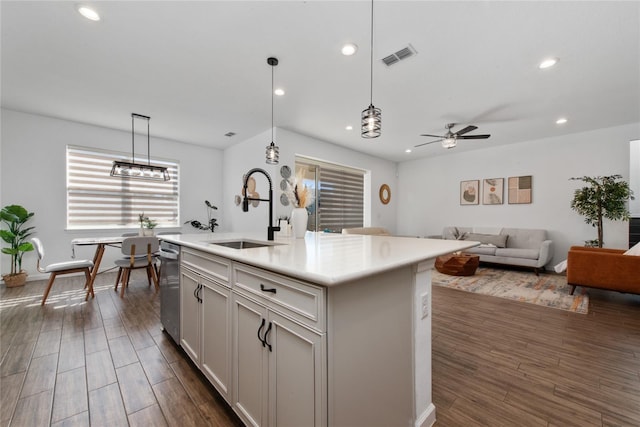 kitchen featuring ceiling fan, a kitchen island with sink, sink, dark hardwood / wood-style floors, and hanging light fixtures