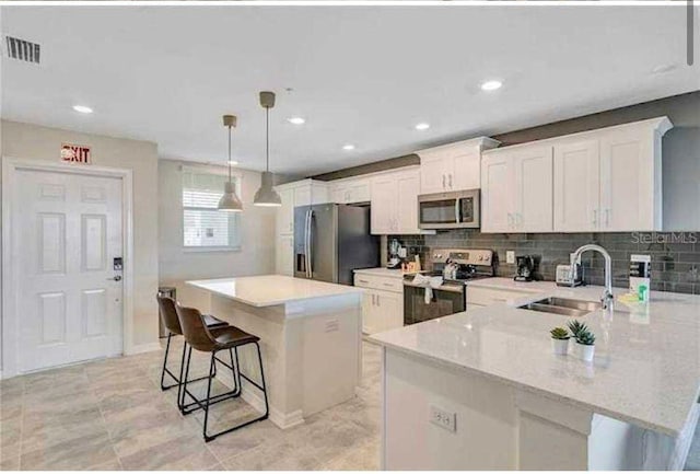 kitchen featuring white cabinetry, sink, hanging light fixtures, stainless steel appliances, and a kitchen island