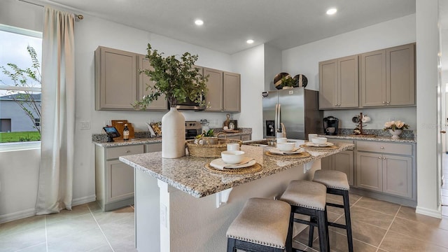 kitchen with light stone counters, stainless steel appliances, a center island with sink, a breakfast bar area, and light tile patterned flooring