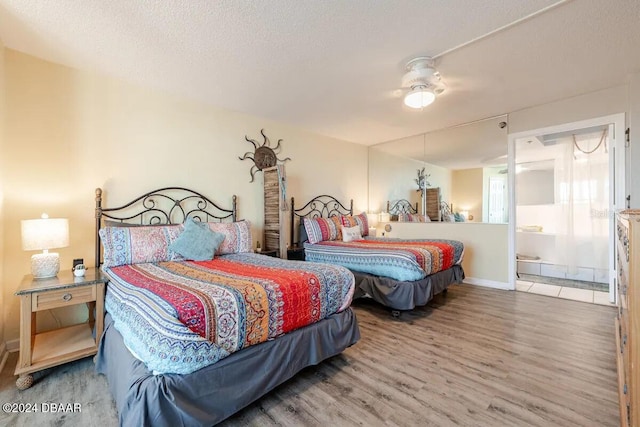 bedroom featuring baseboards, a textured ceiling, ensuite bathroom, and wood finished floors